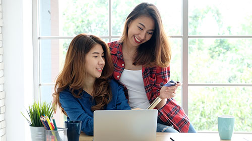 Two young women holding credit card and using laptop comp