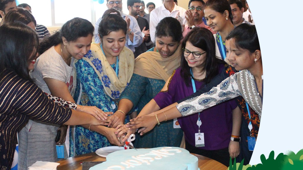 A group of women smiling, cutting into a cake.