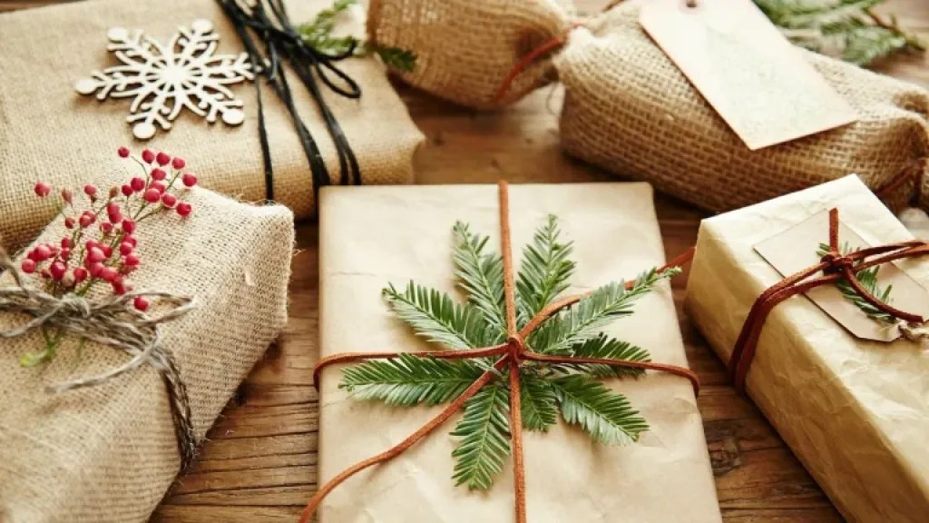 Quattro scatole avvolte in carta regalo marrone con nastri e decorazioni in tema invernale.