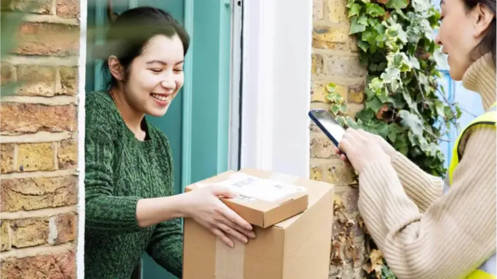 Mulher recebendo pacotes de um entregador com um celular na mão.
